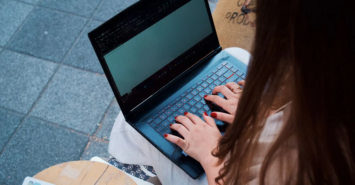 Jeune femme tapant sur un ordinateur portable dans un café en plein air, améliorant l'expérience de travail à distance.