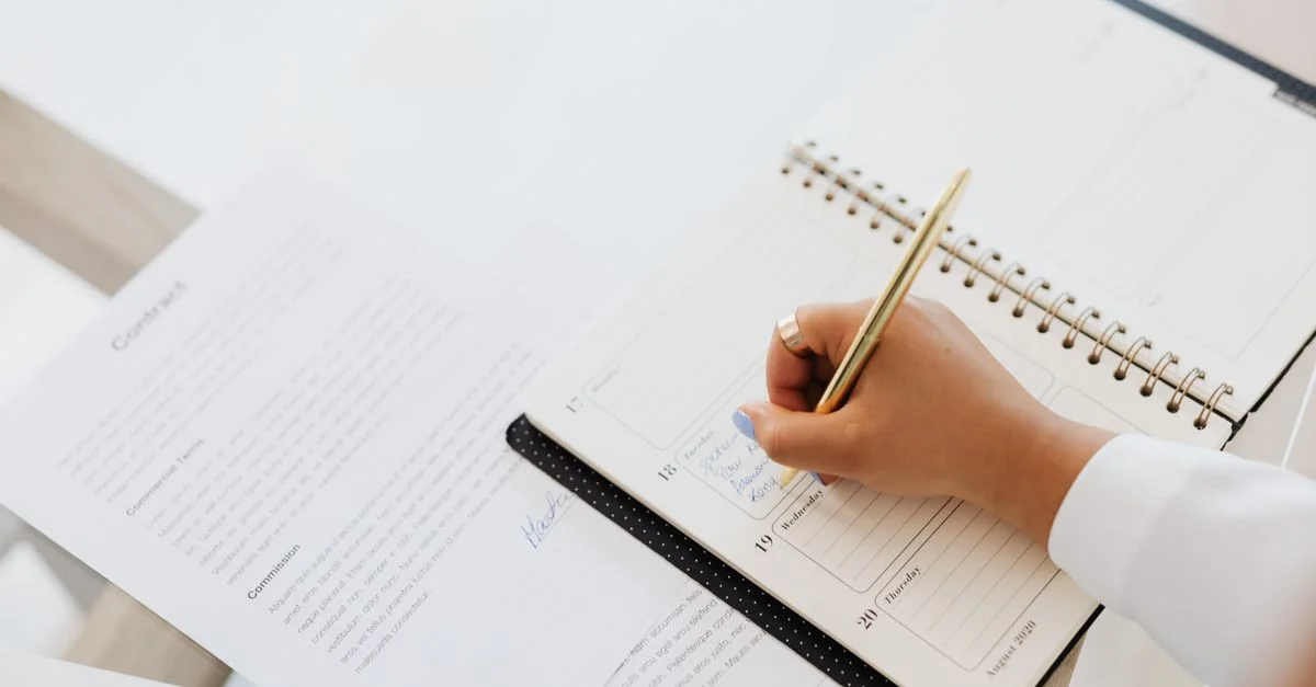 Gros plan sur une personne écrivant dans un agenda à côté d'un document de contrat sur un bureau.
